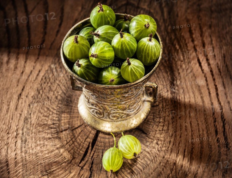 Juicy gooseberries in metal bowl on vintage wood background