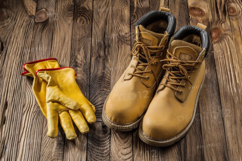 Construction safety tools yellow working gloves and leather working boots on vintage wooden background