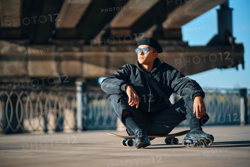 Skater male relax sitting on skateboard on street urban background. Extreme sports concept