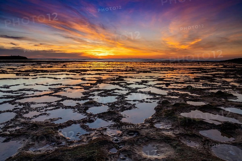 A beautiful sunset over the ocean with rocky beach and tidal pools in the foreground