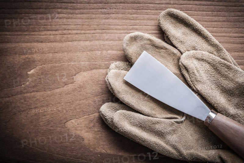 Paint scraper and safety glove on wooden board