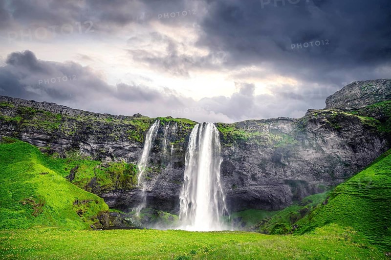 The beautiful Seljalandsfoss waterfall in Iceland surrounded by lava cliffs and green fields in a cloudy sunset