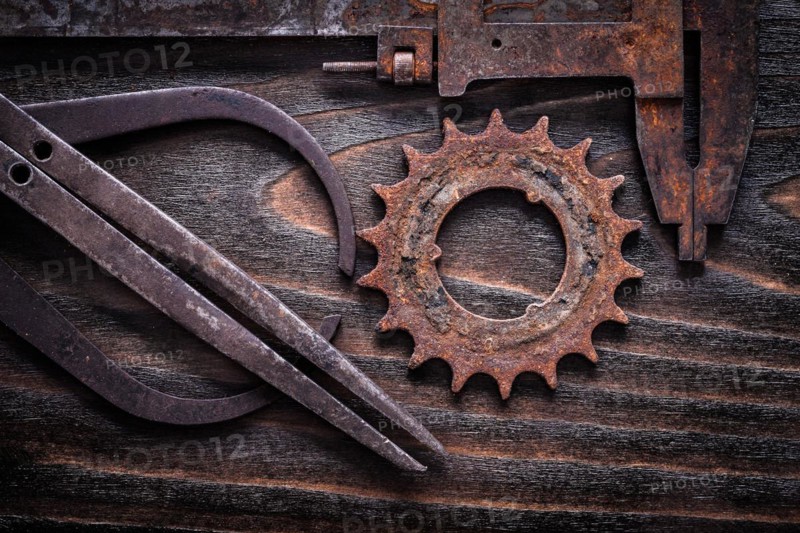 Rusted antique measuring calipers with cog- wheel on vintage dark wooden background close up view construction concept