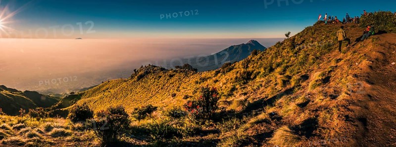 Panoramic photo of mountains surrounding Mount Merbabu and hikers at top during sunrise near Yogya in central Java province in Indonesia. In this region, one can only meet people from isolated local tribes