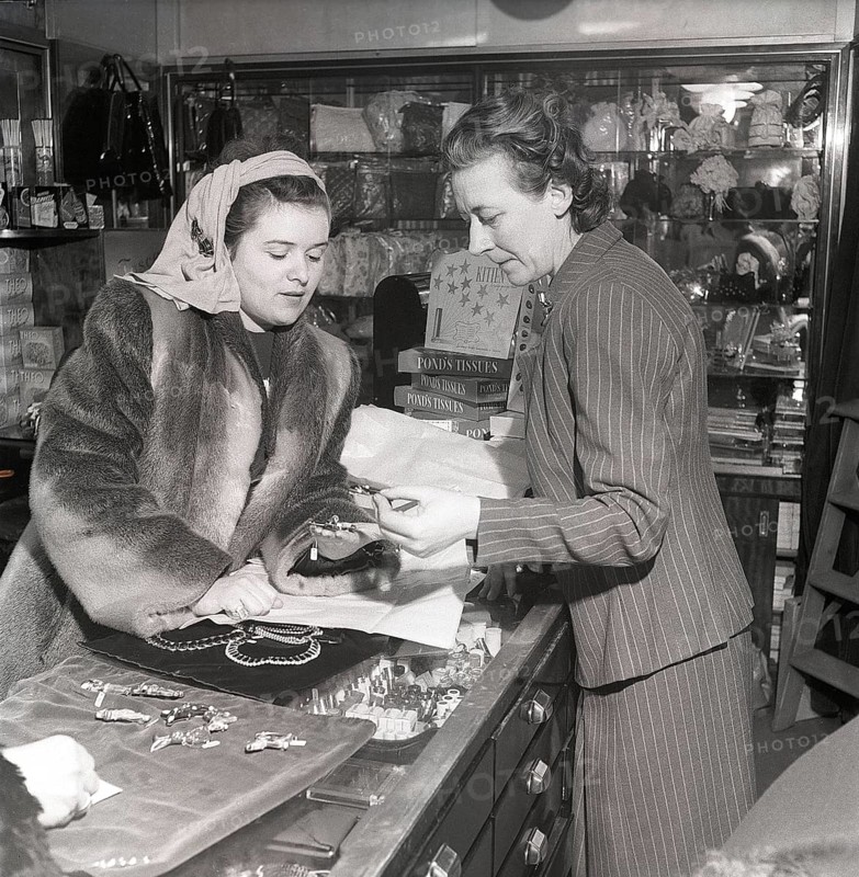 Shopping in the 1940s. A young woman in a store where a sales woman is presenting some of the stores selection of jewellry and charms. On the sales counter products from Pond's tissues is visible. A product marketed as the closest thing to a fine handkerchief, smooth, strong and absorbent. Sweden 1947. Kristoffersson ref AB3-4