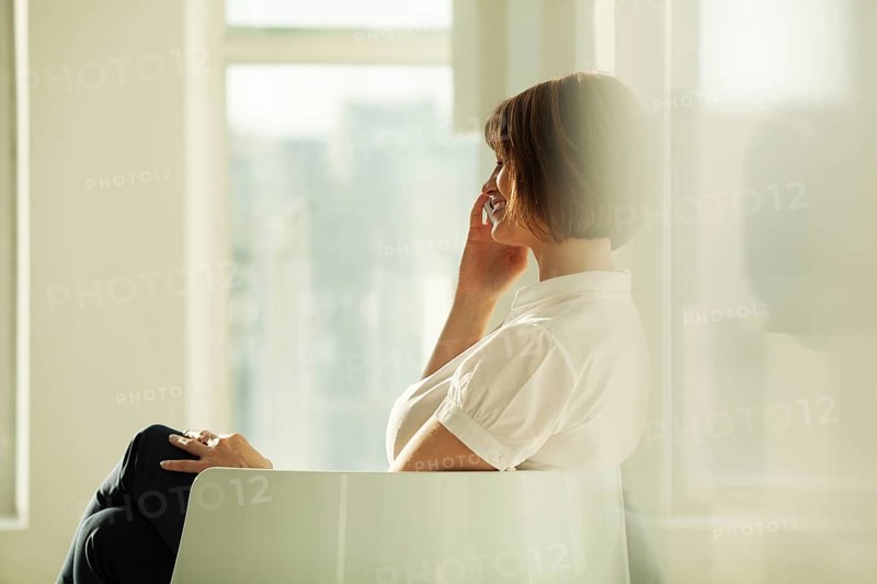 Smiling adult businesswoman talking on smartphone while sitting in chair