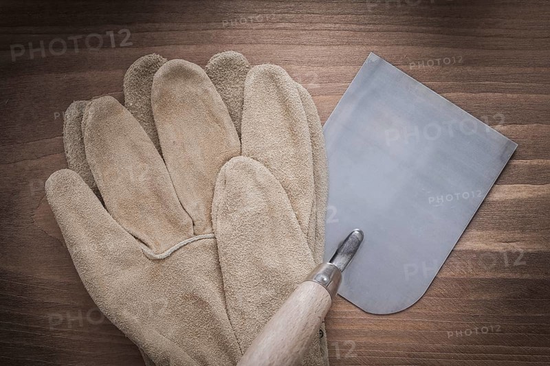 Working safety gloves and bricklaying trowel on vintage wooden background