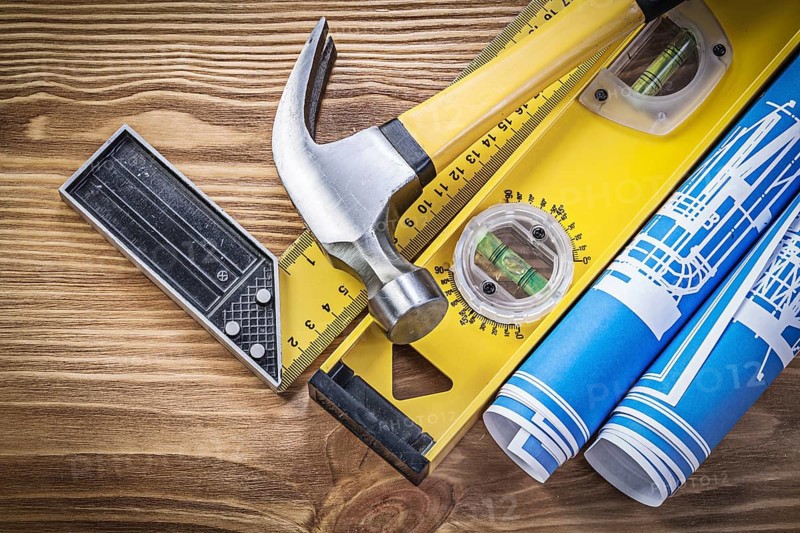 Blue engineering drawings construction level square ruler claw hammer on wooden board