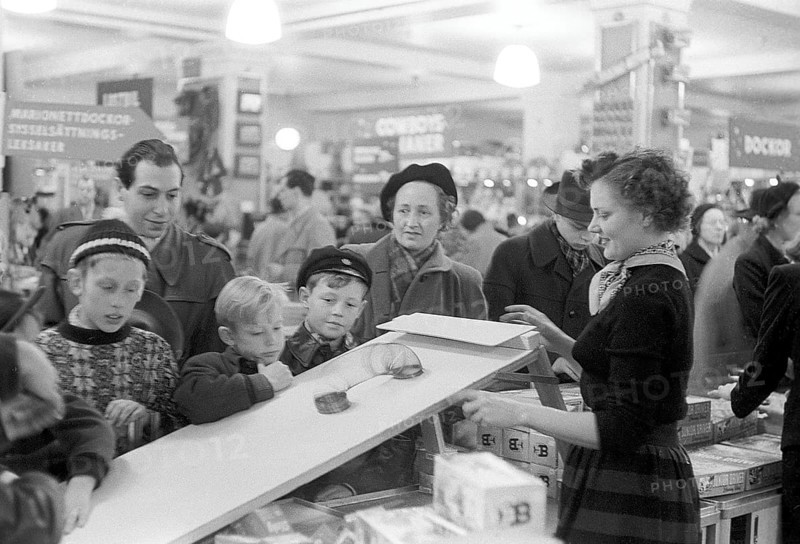 Toys in the 1950s. Interior from the NK department store in Stockholm. A clerk in the toy department shows how the Walking Spring works. A classic toy from the era. The spring was started, for example, on a staircase and then wandered down by itself. The children and adults gathered around the demonstration watch in fascination. Stockholm 1953. Kristoffersson ref 1-2