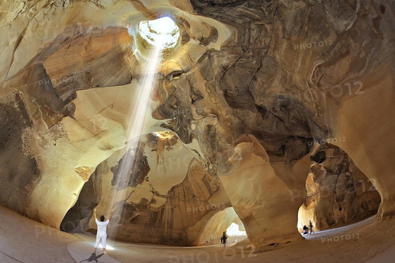 Yoga classes in the cave Beit Guvrin, Israel. Woman in white performs asana Sun salutation