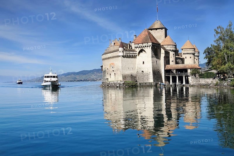 World-wide well-known Château de Chillon on Lake Geneva. The white tourist motor ship floats by a magnificent medieval castle
