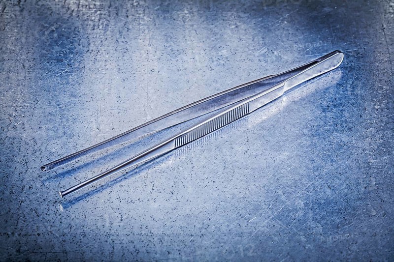 Pair of tweezers on metallic background medicine concept
