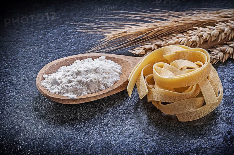 Wheat rye ears wooden spoon flour pasta on black background