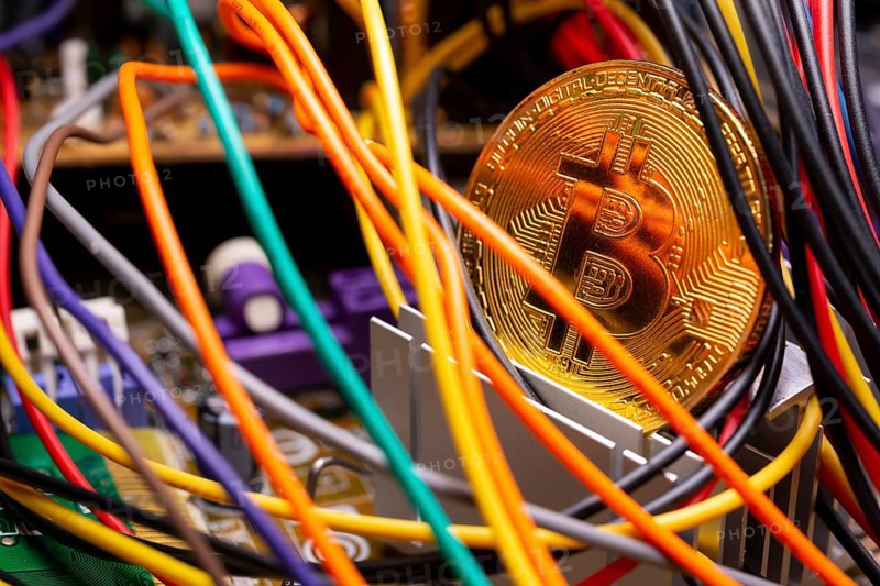 Virtual cryptocurrency money Bitcoin golden coin on a computer printed circuit board PCB surrounded by different colorful cables. The future of money. Computational equipment