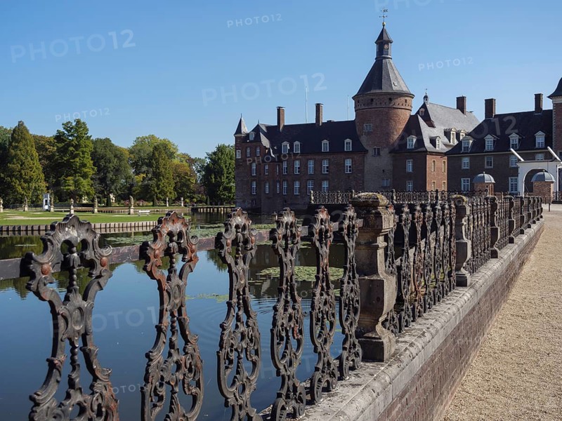Ornate iron fence along a moat with a view of a brick castle, anholt, isselburg, münsterland, germany