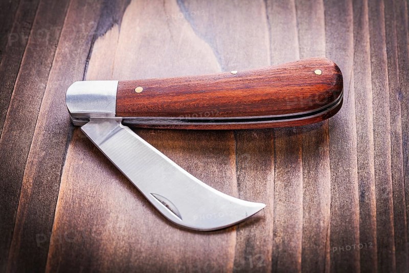 Opened agricultural knife on vintage wooden board close up