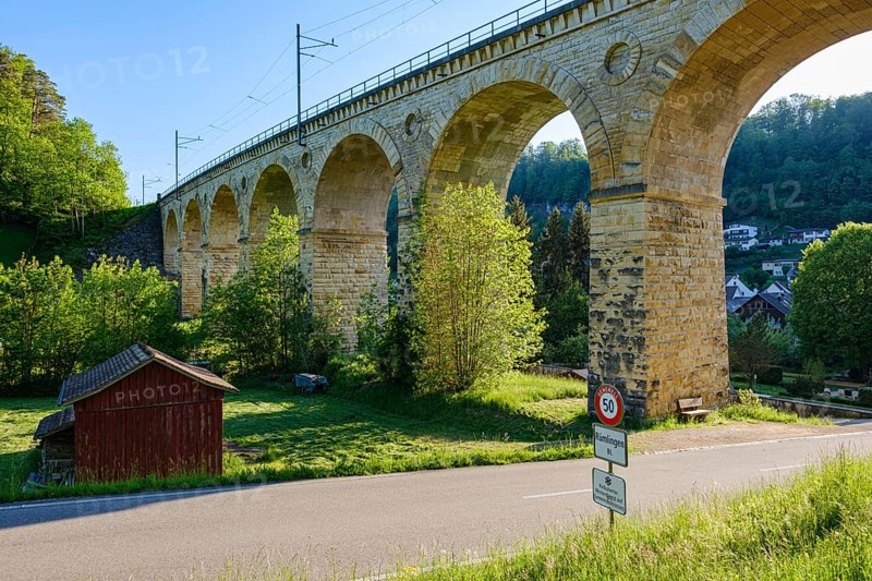 A massive stone viaduct towers over a green landscape with a small country road in the foreground, Rümlingen, Basel-Landschaft, Switzerland, Europe