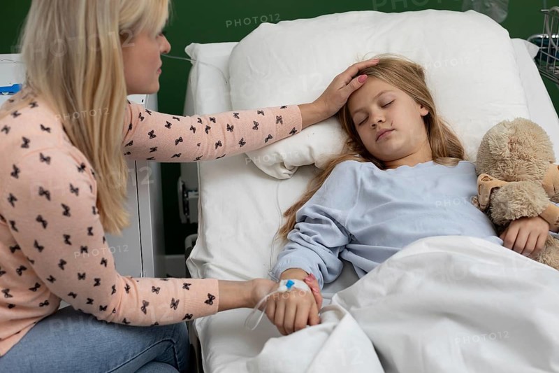 A mother comforts her sick daughter in a hospital bed, showing deep love and support during this tough time