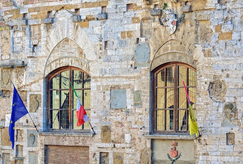 Windows, flags and a coat of arms on the facade of Palazzo Nuovo del Podesta in San Gimignano, Italy, Europe