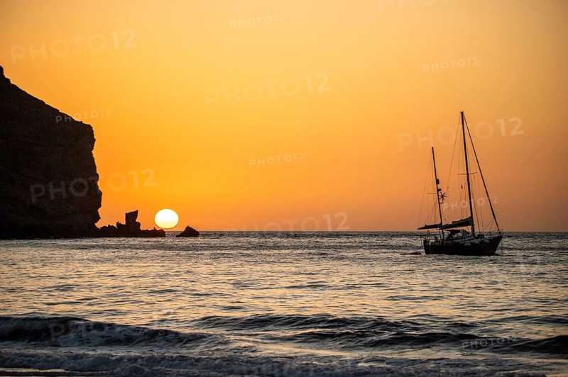 Sunrise during a storm, Calima. A haze-covered horizon turns orange as the sun rises as a ball. A boat is anchored in the sea. Landscape photograph in Gran Tarajal, Canary Islands, Spain, Europe