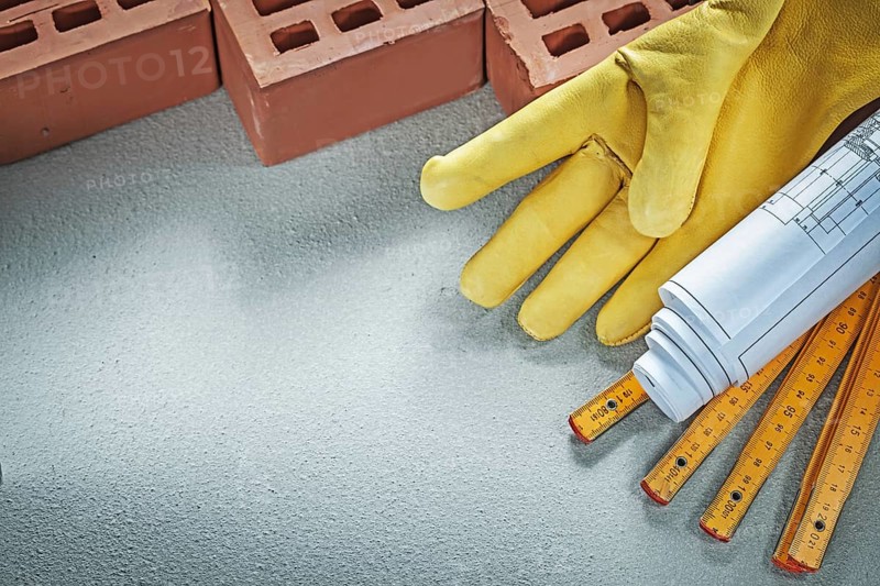 Red bricks safety gloves blueprints wooden meter on concrete background building concept