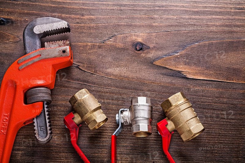 Plumbers fixtures with red handles and monkey wrench on vintage wooden board with copyspace construction concept