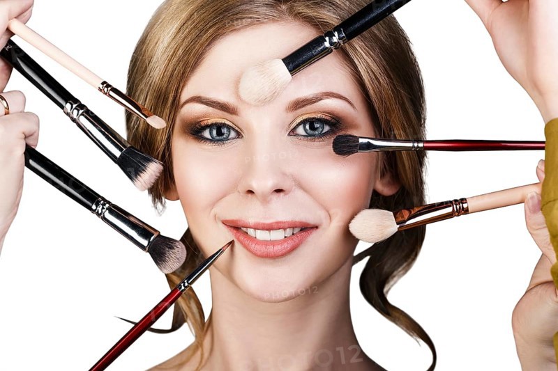 Many hands with cosmetics brushes doing make-up to glamour woman, over white background