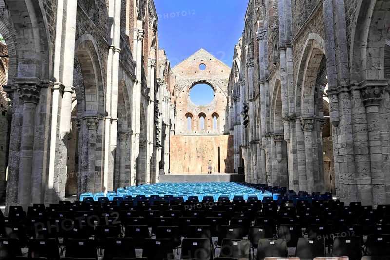Church ruins of the Cistercian Abbey of San Galgano, Abbazia San Galgano, Gothic, Chiusdino, Tuscany, Italy, Europe, Interior of a ruined church with rows of chairs facing forwards, open stone arches and blue sky above, Europe