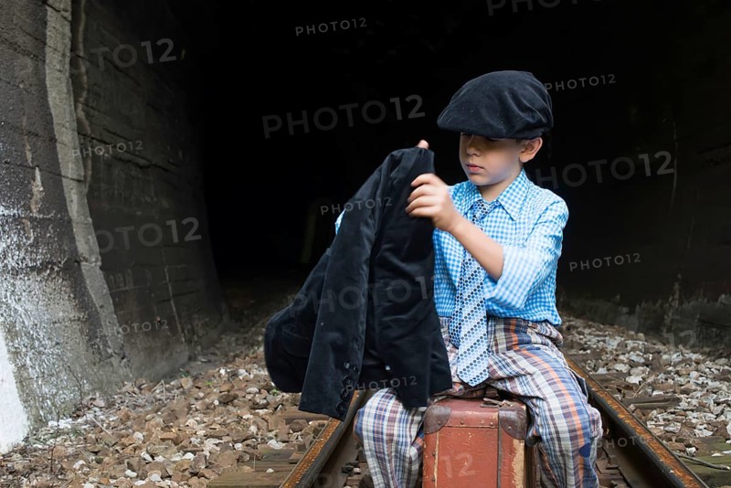 Child in vintage clothes sits on railway road in front of a tunnel