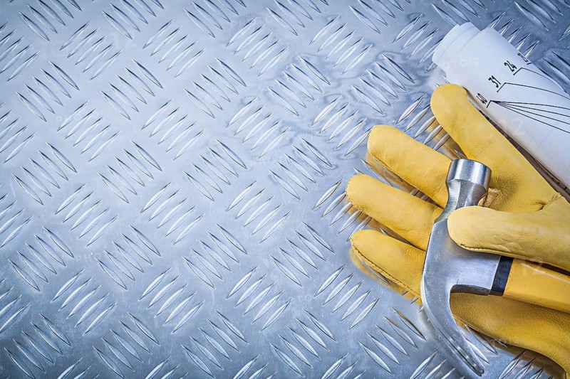 Claw hammer protective gloves rolled engineering drawings on grooved metal plate copy space construction concept