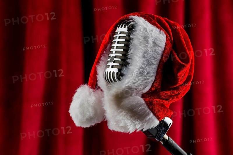 An old retro microphone with a Christmas hat in front of a red velvet background. Austria