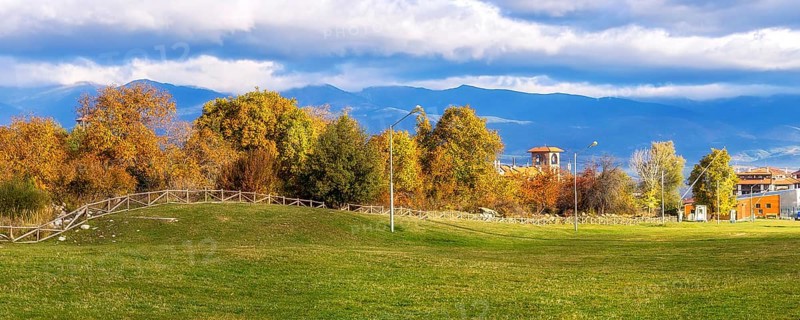 Bansko, Bulgaria autumn panorama banner background with colorful green, red and yellow trees, Rila mountains and house tower