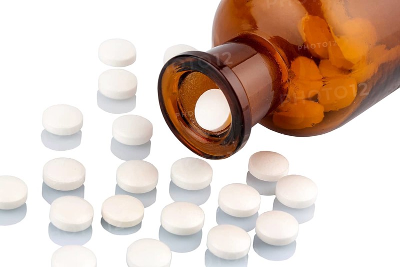 Many tablets with a glass container. Symbolic photo for addiction and costs in medicine and medication. Austria