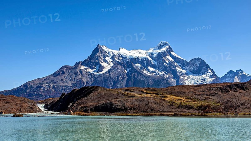 Snowy mountain above a calm river and turquoise water under a blue sky, The landscape of the Torres del Paine National Park in Patagonia in Chile
