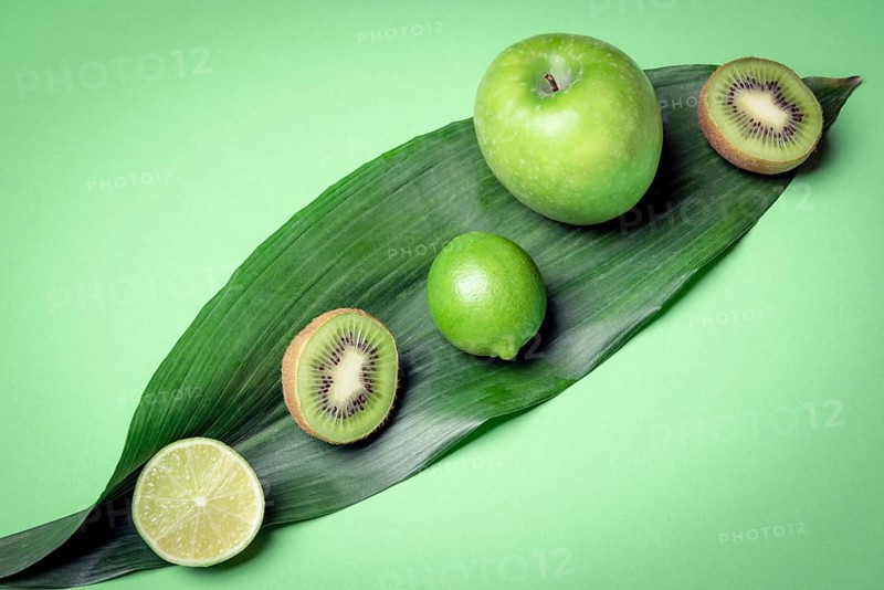 Mix of raw fruits on a green leave. Green kitchen table with fresh detox fruits