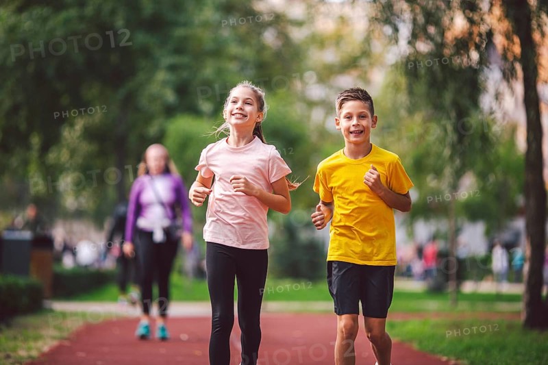 Sports and fitness in adolescence. Caucasian twins boy and girl run on the jogging track in the city park. Two children brother and sister for 10 years running on a rubberised outdoor treadmill