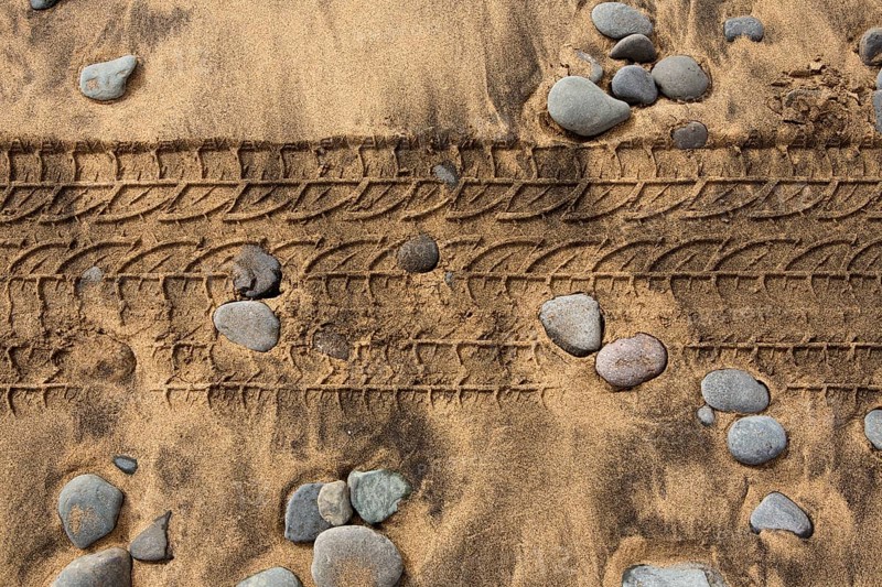 Car tire footprint in a sand and rolling stones beach texture