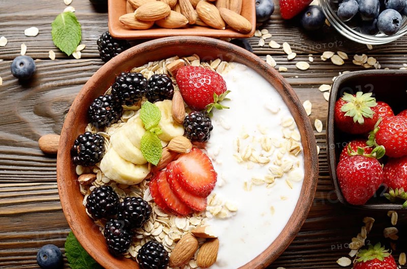 Flat lay top view at Fruit healthy muesli with banana strawberry almonds and blackberry with yogurt in clay dish on wooden kitchen table