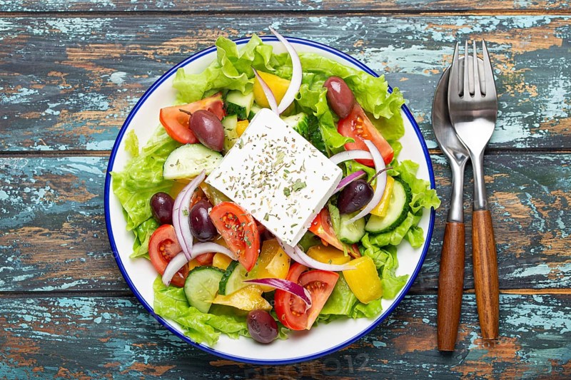 Traditional Greek Salad with Feta Cheese, Tomatoes, Bell Pepper, Cucumbers, Olives, Herbs in white ceramic bowl on blue rustic wooden table background from above, Cuisine of Greece, food photography, food photography