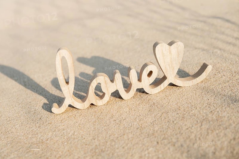 Wooden word love on sandy beach background. Concept of romantic holiday anniversary, proposal, valentines day greeting card, postcard. Letter text in tropical vacation Sand surface. Deep shadows Love is all you need