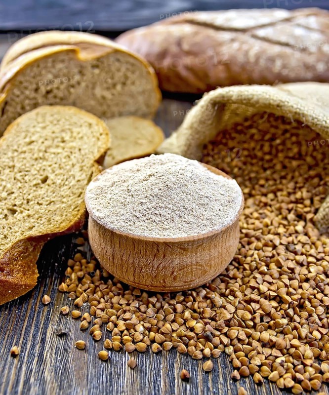 Buckwheat flour in a wooden bowl, buckwheat in the bag, the bread slices on a wooden boards background