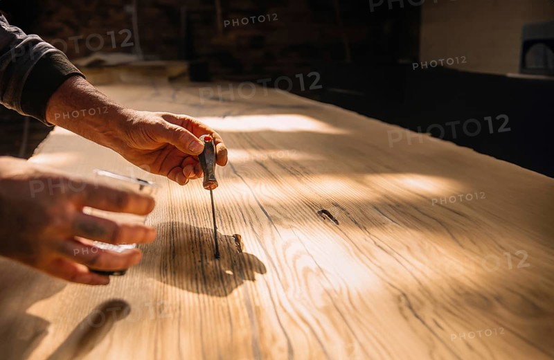 Person using tools on wood in a workshop with warm sunlight creating a focused and serene atmosphere
