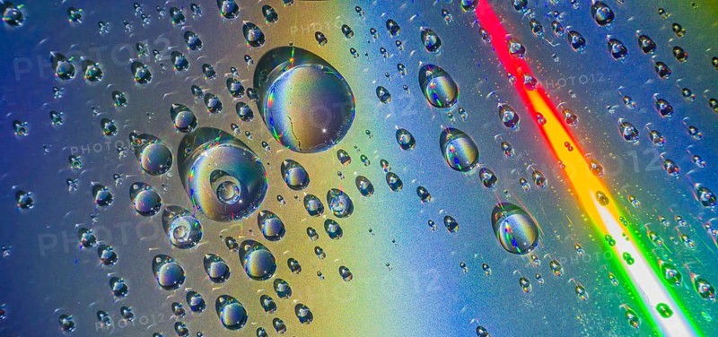 Beautiful closeup of water droplets floating on blueish silver background with rainbow colors dissecting the background