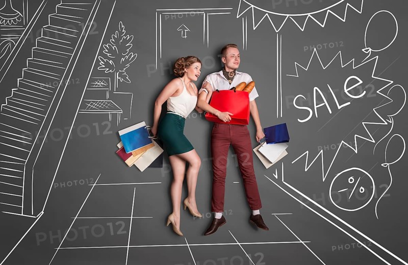 Love story concept of romantic couple shopping against chalk drawings background. Young happy couple standing together with shopping bags in a shopping centre during a sale