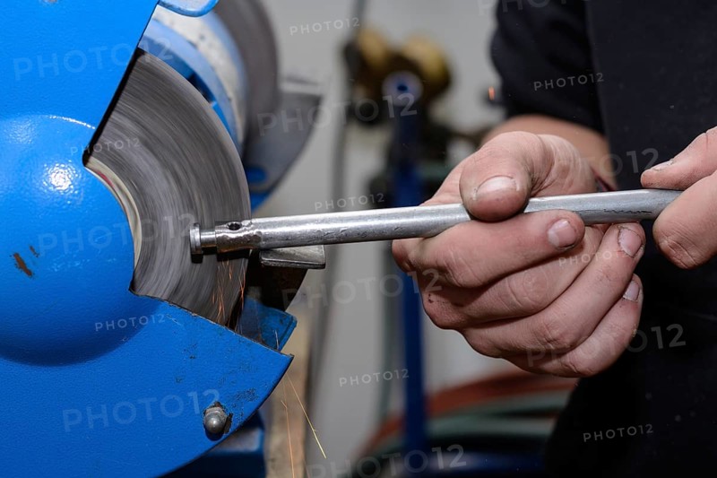 Skilled worker working on metal on a bench grinder - close-up