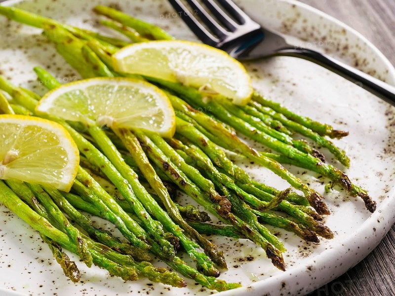 Close up view of grilled asparagus and slice of lemon in craft trendy plate on brown wooden table