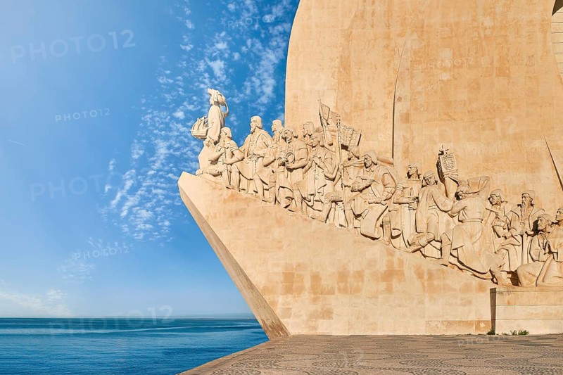 Lateral view of Monument of Discoveries, Padrao dos Descobrimentos, to Age of Discoverys haped as ship with statues of Prince Henry the Navigator and great people of Portuguese seafarers history, Lisbon, Portugal, at clear blue sky and sunrays on day, Europe