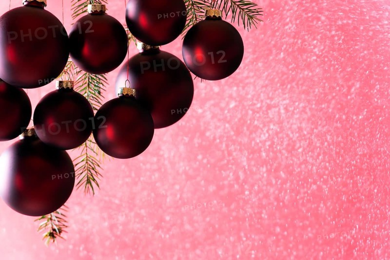 Elegant dark red Christmas balls hanging while snowing, from a snow spray, in bright light, perfect for a Christmas greeting card or banner