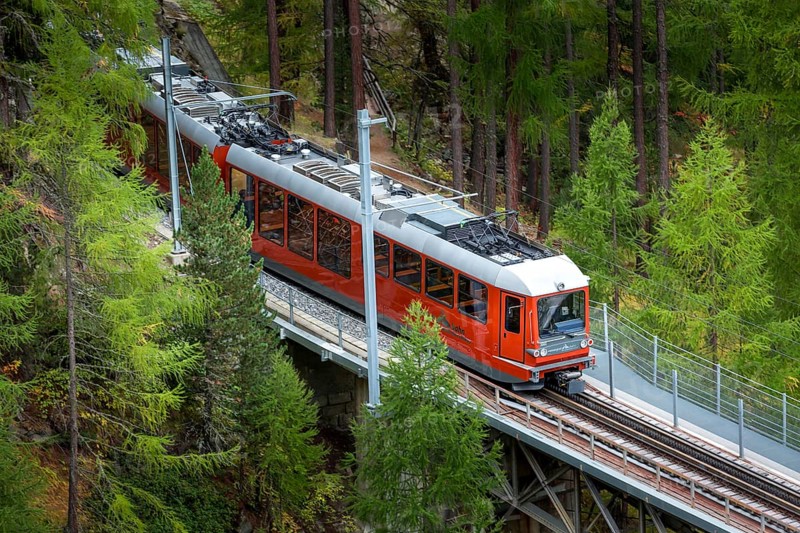 Zermatt, Switzerland, October 7, 2019: Gornergrat red tourist train on the bridge, village houses and Swiss Alps panorama, Europe