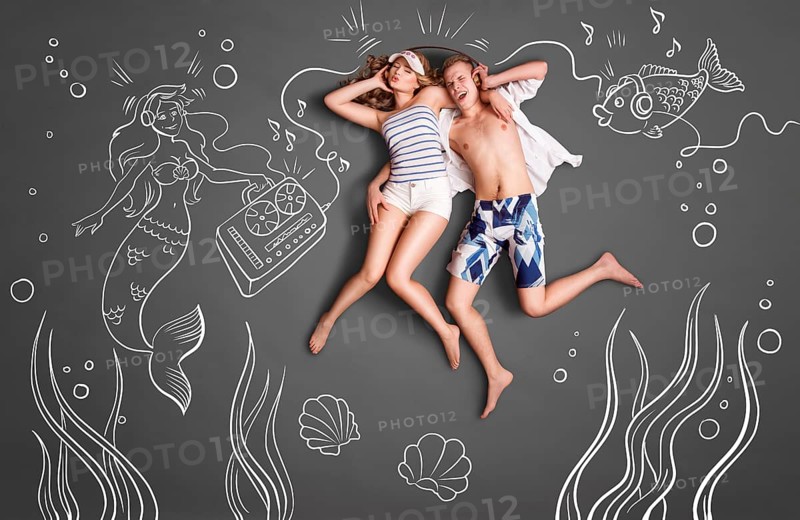 Happy valentines love story concept of a romantic couple swimming underwater, sharing headphones, and listening to music against chalk drawings undersea background
